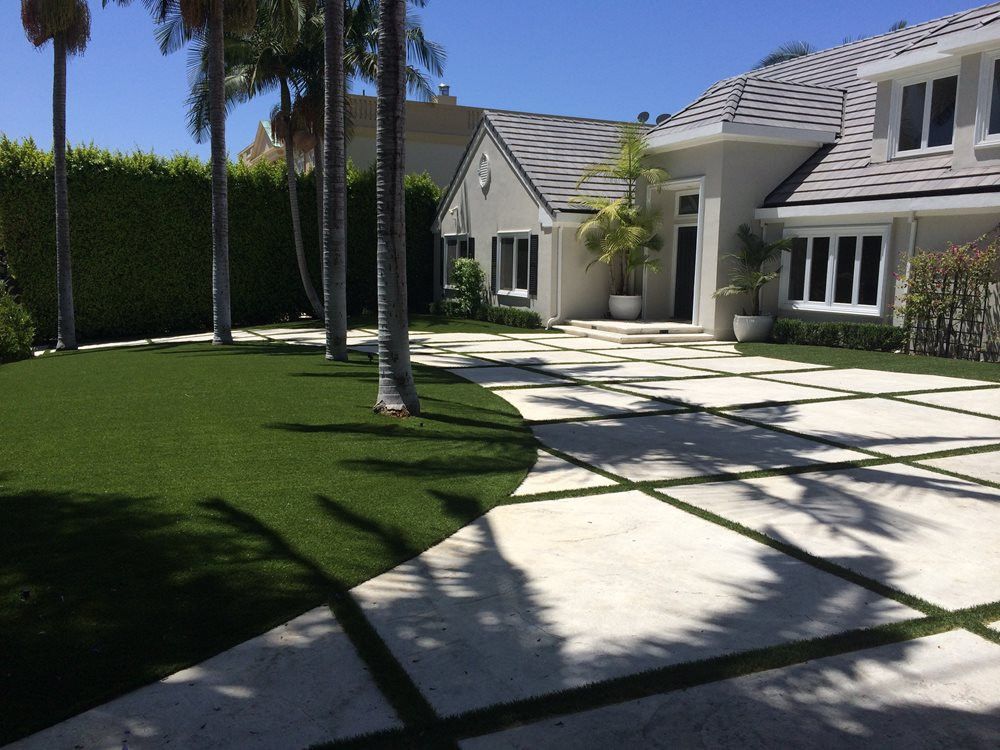 artificial turf in front of a house with pavers and a driveway